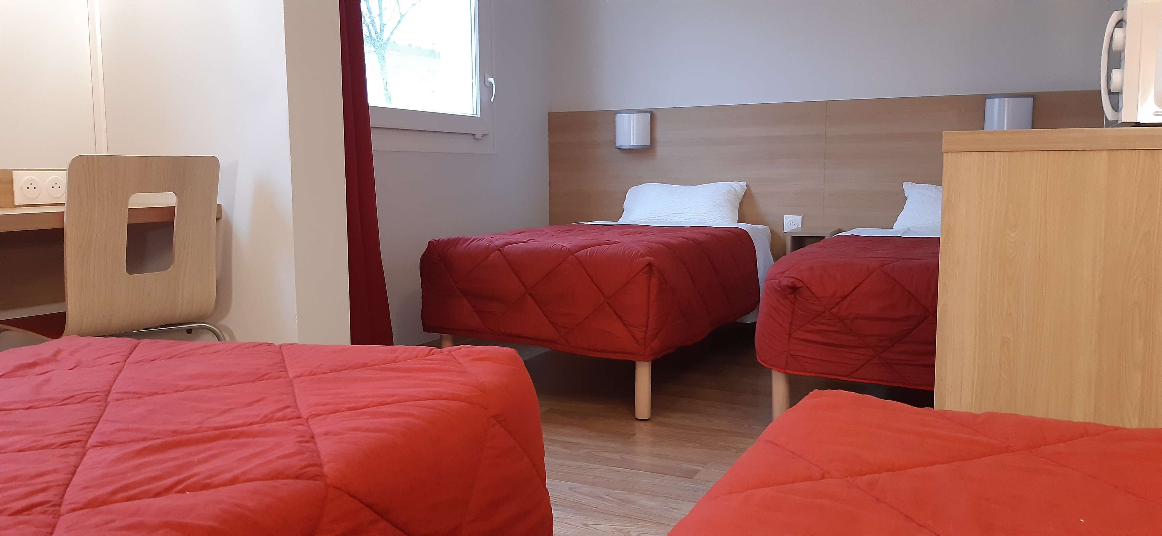 Habitación de hotel con dos camas individuales, un escritorio de madera y una silla.