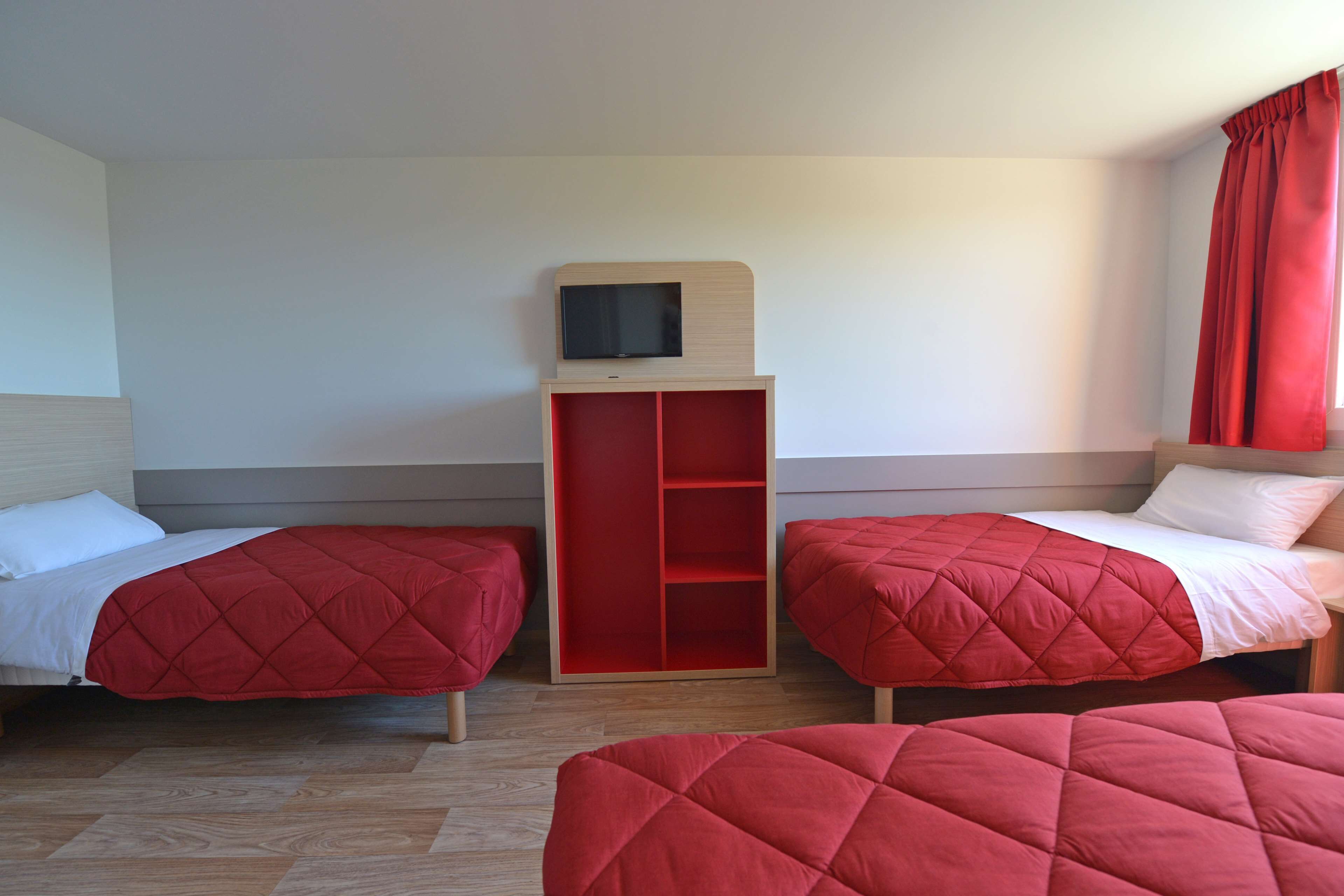 Une chambre d’hôtel avec deux lits, un téléviseur posé sur un meuble et une armoire rouge.