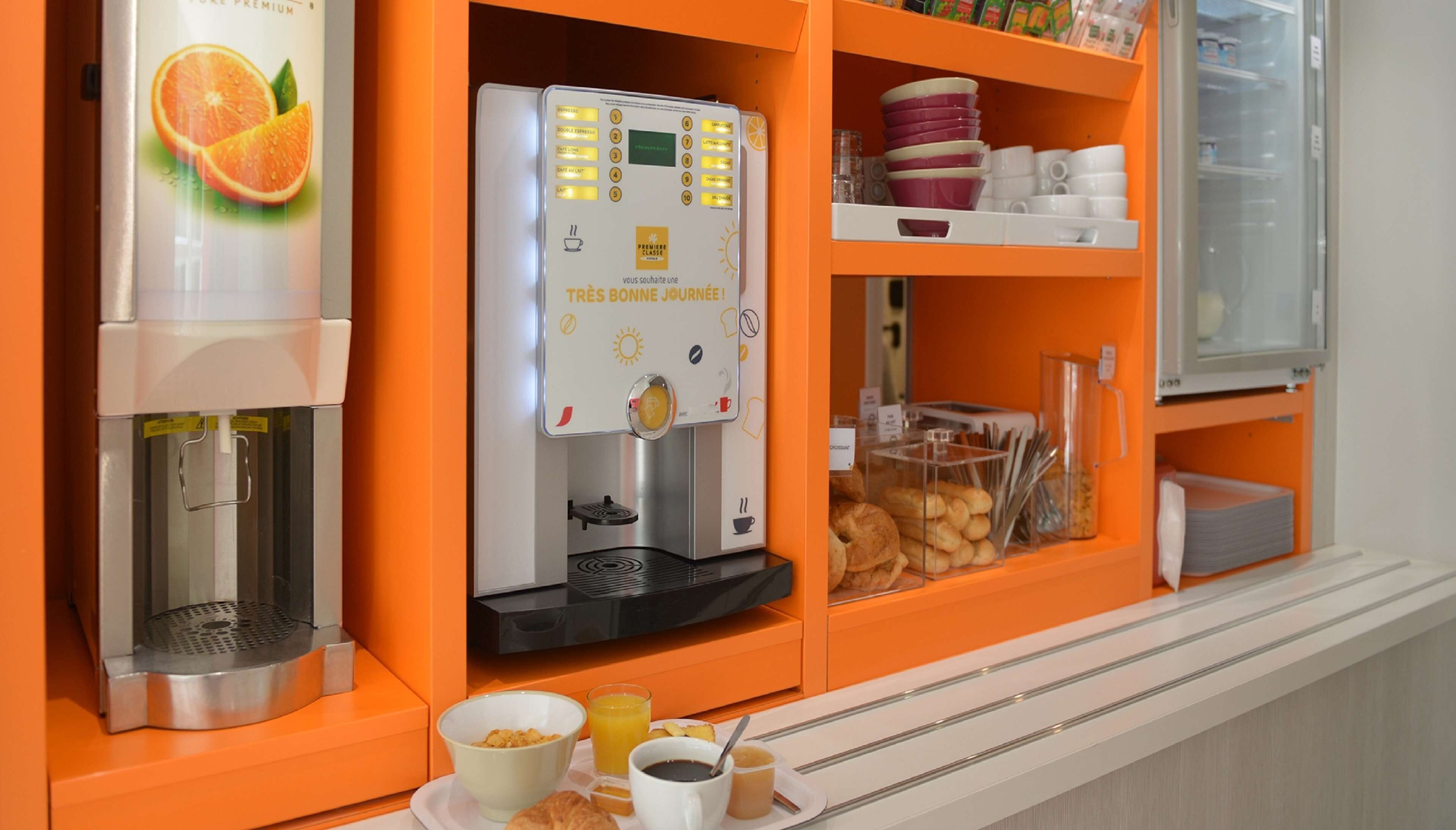 Een ontbijtbuffet met een koffieapparaat, sinaasappelsapautomaat en diverse ontbijtartikelen, waaronder gebak en brood.