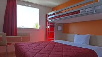 A bunk bed room with a red bedspread, a desk with a chair, and a window with red curtains.