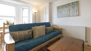 A living room with a blue sofa, a wooden coffee table, and a painting on the wall. - Sleep & Stay Oxford - Beautiful Flat Close to town (Oxford)