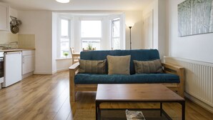 A modern living room with a blue sofa, a wooden coffee table, and a kitchen area with white cabinets and a stove. - Sleep & Stay Oxford - Beautiful Flat Close to town (Oxford)