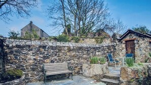 A stone-walled courtyard with a bench, a small table, and a chair.