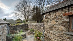 A stone building with a stone pathway leading to a small garden area with plants and a wooden fence.