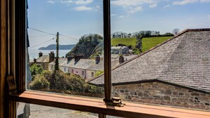 A view from a window overlooking a coastal area with stone buildings, a grassy hill, and a body of water.