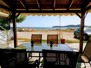 Ein überdachter Außenbereich mit Tisch und Stühlen, der auf einen Strand mit einem in der Nähe stehenden Auto blickt.