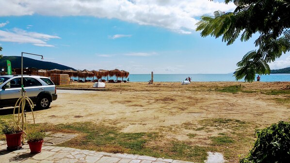 Ein Strand mit einem geparkten Auto, einem Gebäude mit einem Reetdach und einigen Personen.