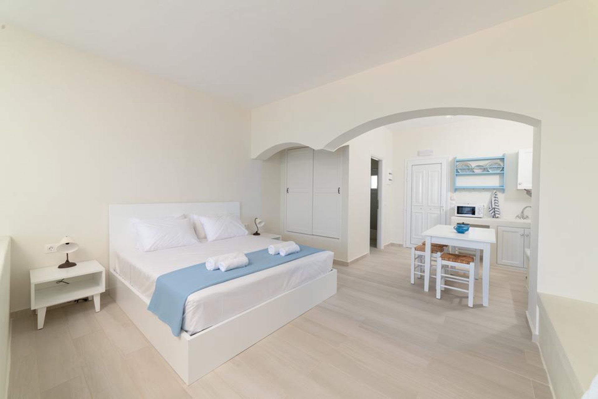 Een slaapkamer met een bed, nachtkastje, bureau en kitchenette.