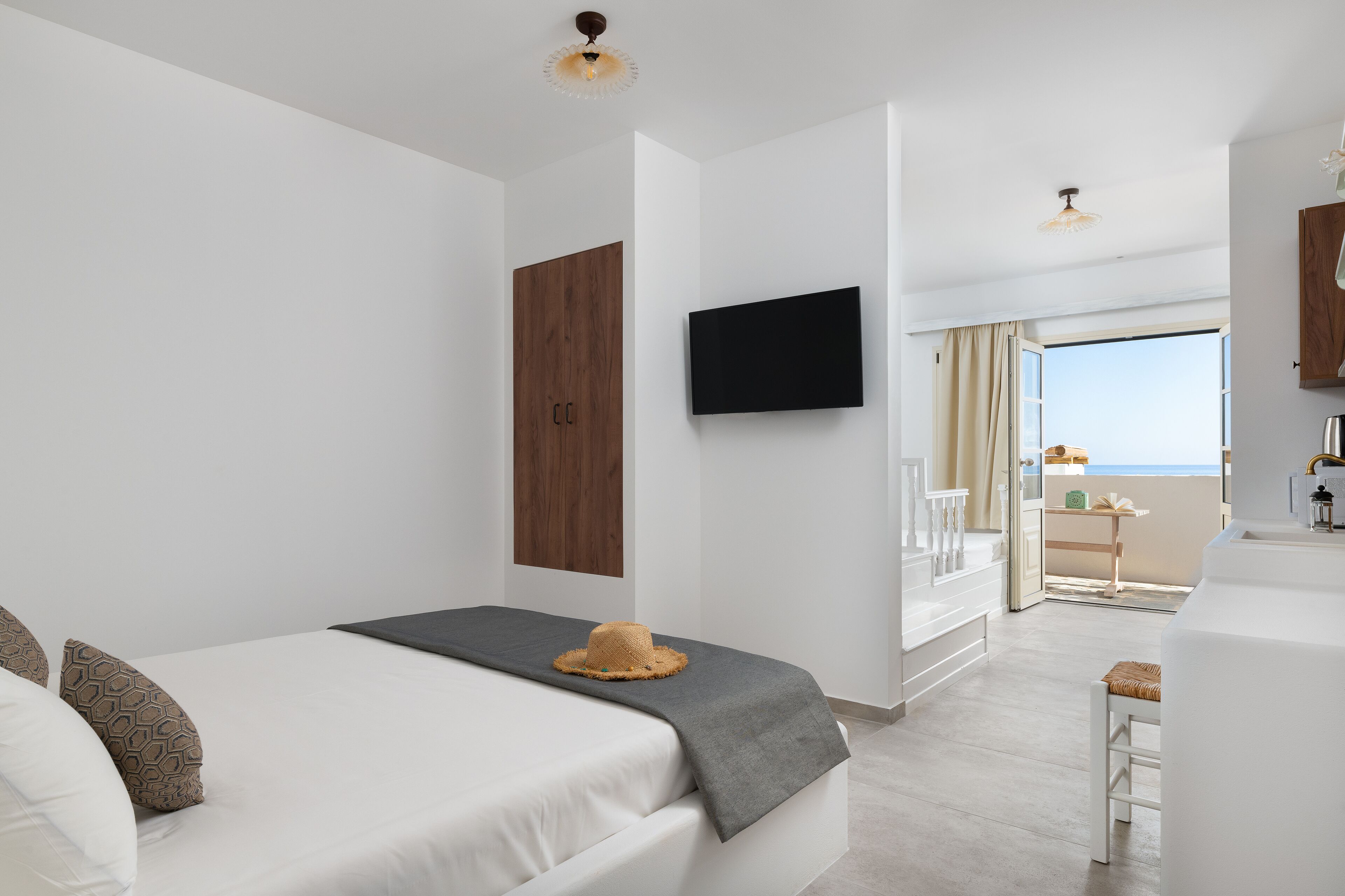 Una habitación de hotel moderna con cama, televisión, balcón con vistas y una pequeña cocina.