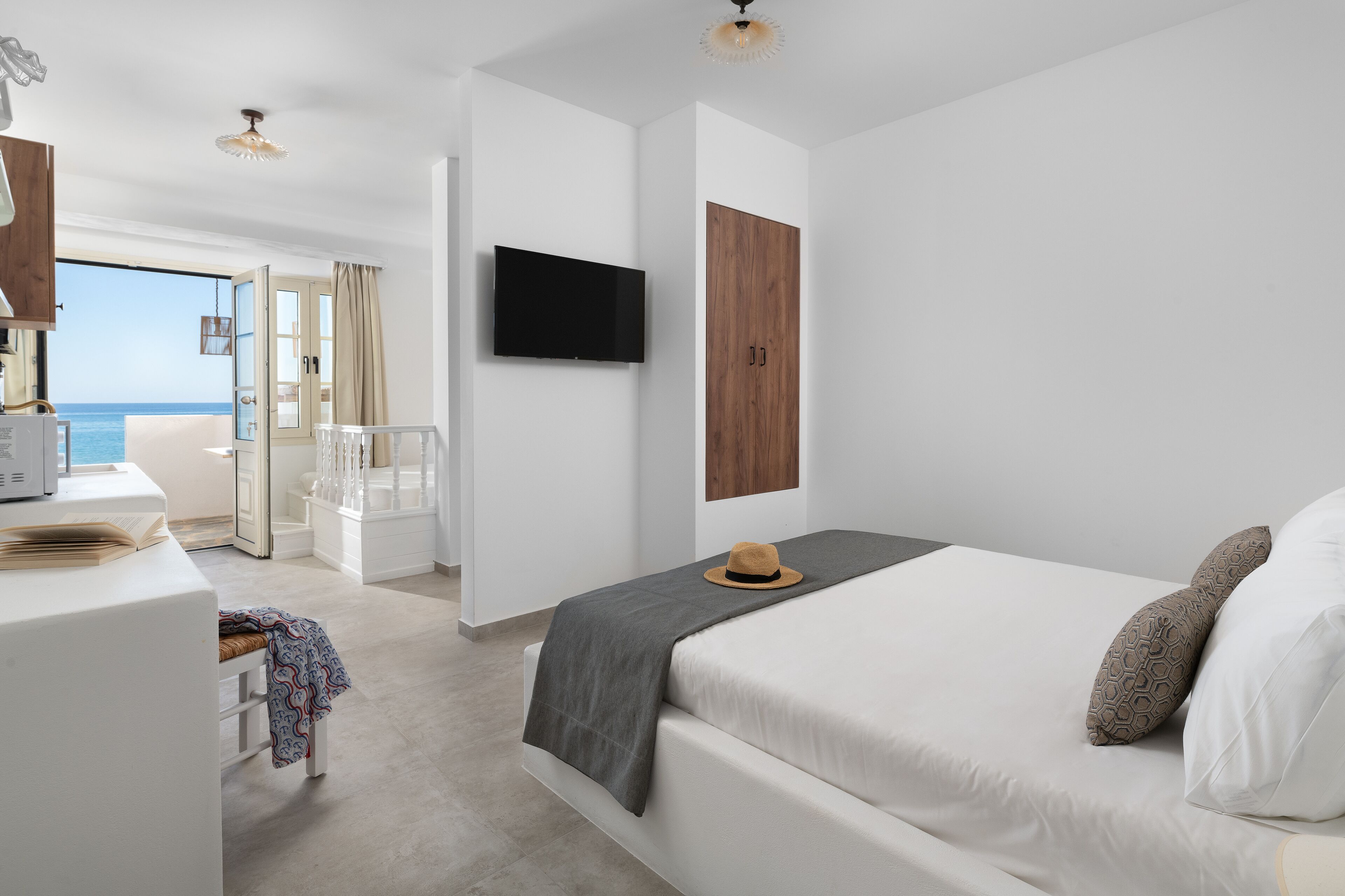 Ein modernes Hotelzimmer mit Bett, Fernseher, Holzschrank und Blick aufs Meer.