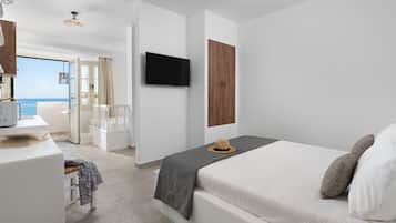 Ein modernes Hotelzimmer mit Bett, Fernseher, Holzschrank und Blick aufs Meer.