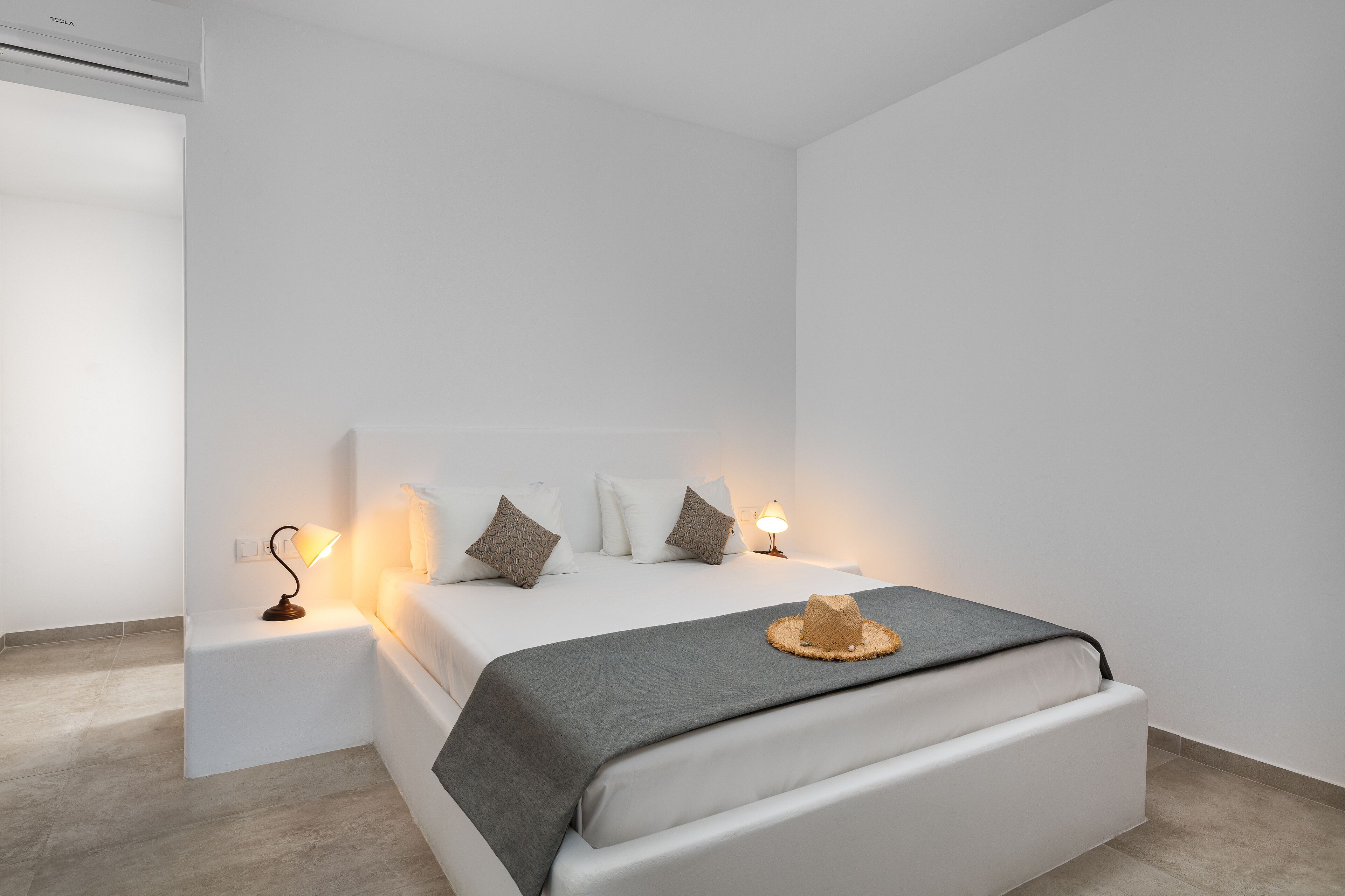 Un dormitorio moderno con una cama grande, paredes blancas y una mesita de noche pequeña con una lámpara.