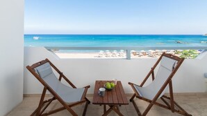 A balcony with two wooden chairs and a small table, overlooking a beach with clear blue water and a boat in the distance. - Stegna Akti (Rhodes)