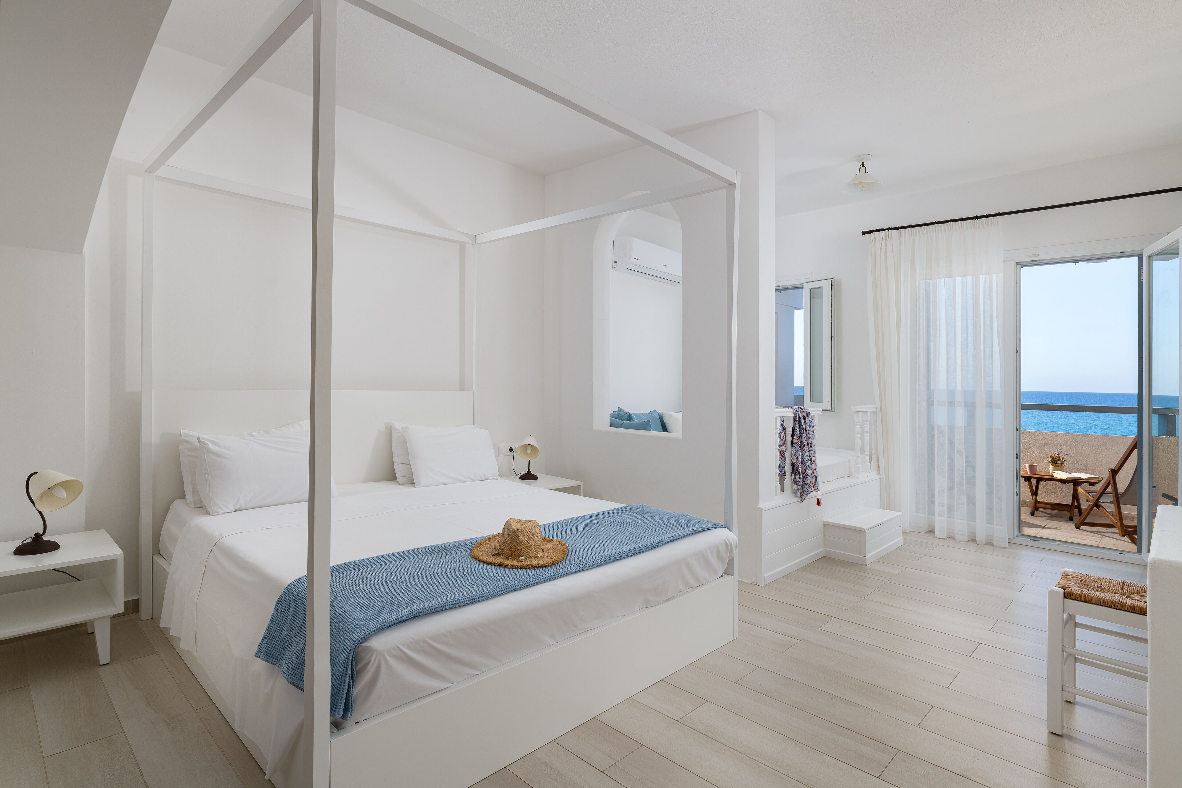 Ein Schlafzimmer mit Himmelbett, einem Balkon mit Meerblick und einer kleinen Sitzecke.