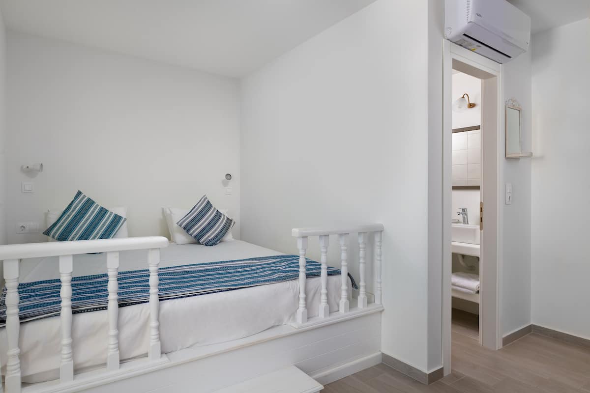 A bedroom with a bed, white railings, a bathroom with a sink and mirror, and an air conditioning unit.