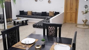 A modern living room with a sofa, dining table set for four, and a staircase leading to another level. - Relax in the comfort of Dar Elyas: our villa with swimming pool in Djerba! (Mezraya)