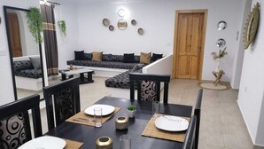 A modern living room with a sofa, dining table set for four, and a staircase leading to another level. - Relax in the comfort of Dar Elyas: our villa with swimming pool in Djerba! (Mezraya)