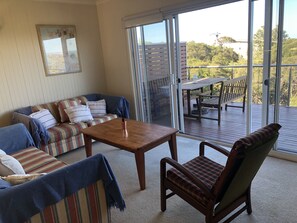 Relax in this inviting living room with a sofa, armchair, and coffee table, leading to an outdoor deck with a table and chairs.