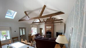 Ein Wohnzimmer mit freiliegenden Holzbalken, einem Kamin, einer Couch und einem Essbereich mit Tisch und Stühlen.