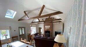 Ein Wohnzimmer mit freiliegenden Holzbalken, einem Kamin, einer Couch und einem Essbereich mit Tisch und Stühlen.