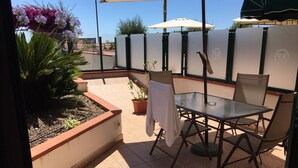 An outdoor patio with a glass table and chairs, surrounded by potted plants and a decorative fence.