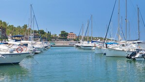 Una marina con varias embarcaciones amarradas, agua tranquila y un edificio al fondo.