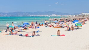 Una playa concurrida, con gente tomando el sol y nadando, sombrillas y sillas de playa.