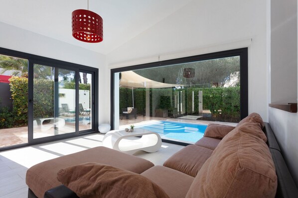 A modern living room with a large glass door leading to a pool area, a white coffee table, and a red pendant light.