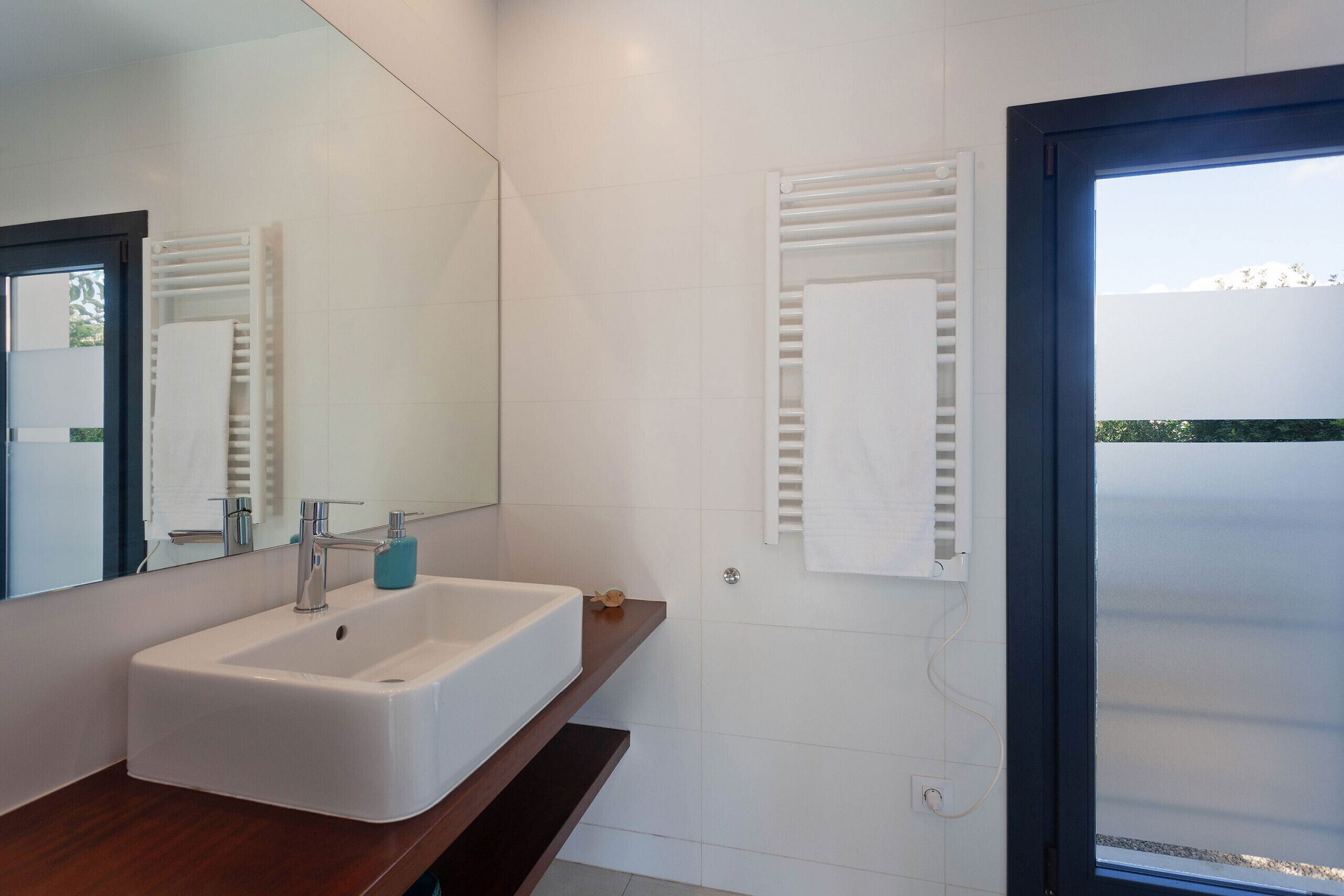 Une salle de bain moderne avec un lavabo blanc, un miroir et un porte-serviettes.