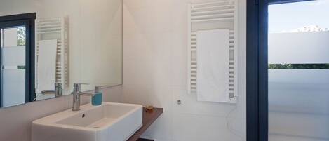 Une salle de bain moderne avec un lavabo blanc, un miroir et un porte-serviettes.