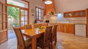 A kitchen with wooden cabinets, a dining table with wicker chairs, and a view of the outdoors. - Casa Fortuny in Soller (Sóller)