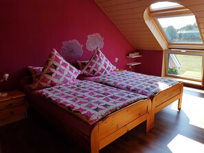 Un dormitorio con techo inclinado, tragaluces, cama con colcha estampada y mesita de noche con lámpara.