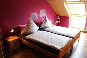 Quarto com cama de madeira, almofadas estampadas, mesa de cabeceira com abajur e claraboia.
