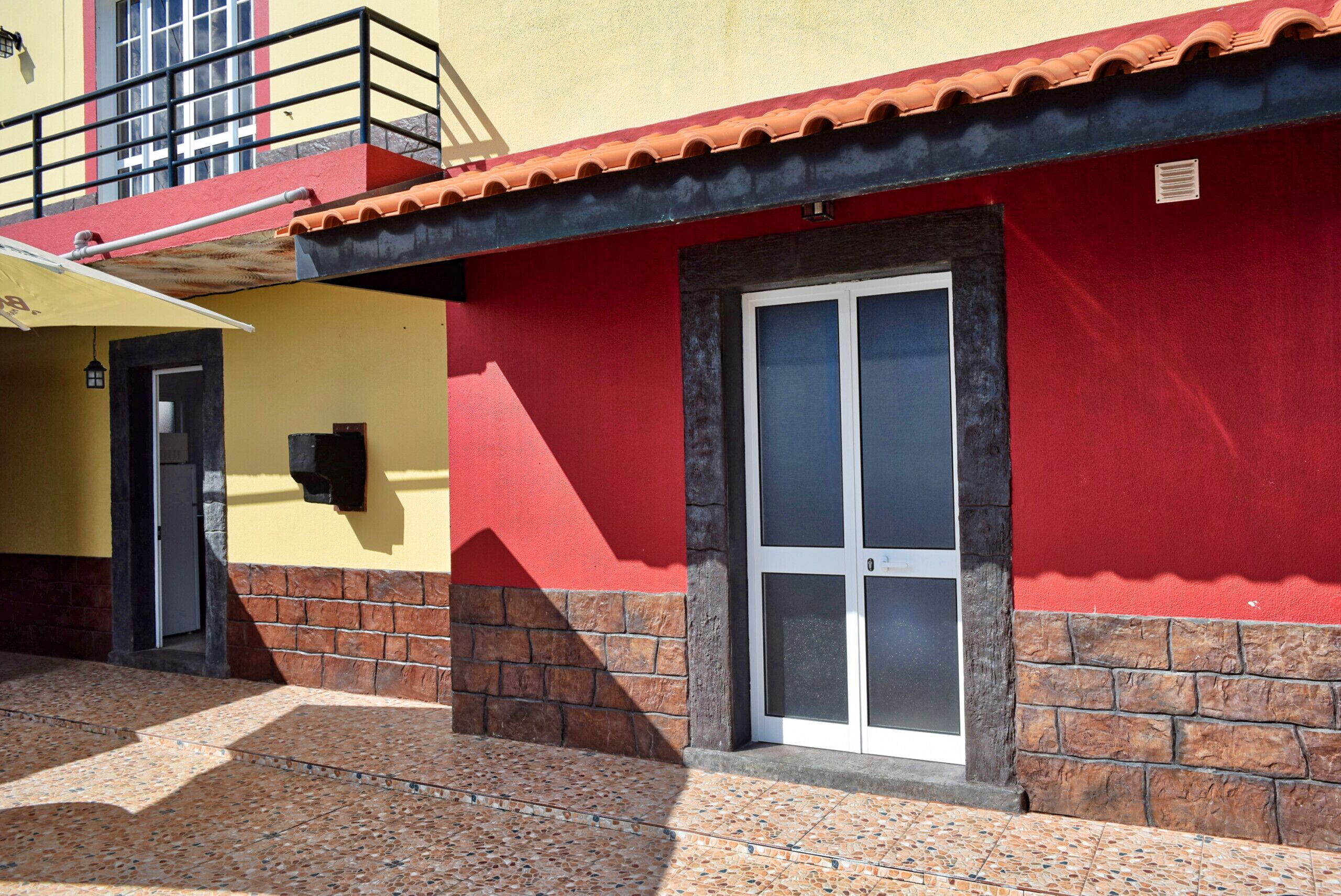 A building with a red and yellow facade, a tiled entrance, and a visible door.