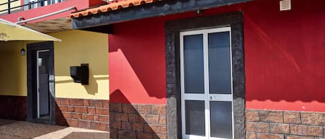 A building with a red and yellow facade, a tiled entrance, and a visible door.