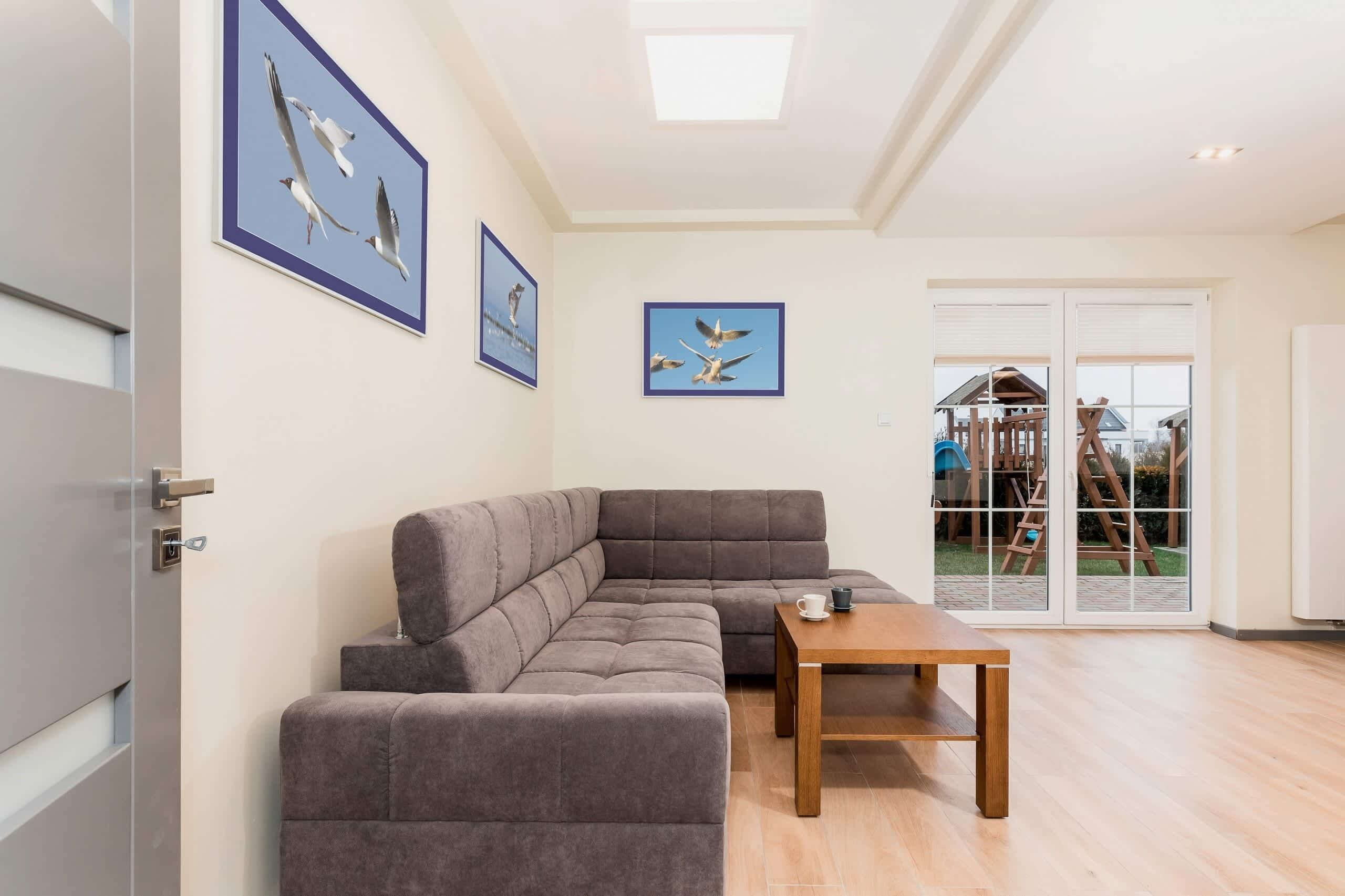 A modern living room with a sectional sofa, a wooden coffee table, and framed bird artwork on the walls.