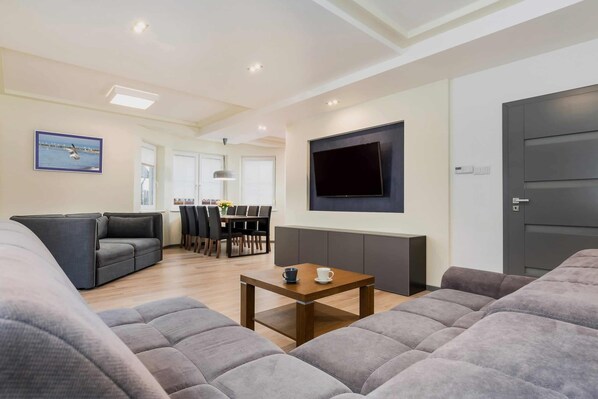 Una sala de estar moderna con un sofá, una mesa de centro, un televisor de pantalla plana y una zona de comedor al fondo.