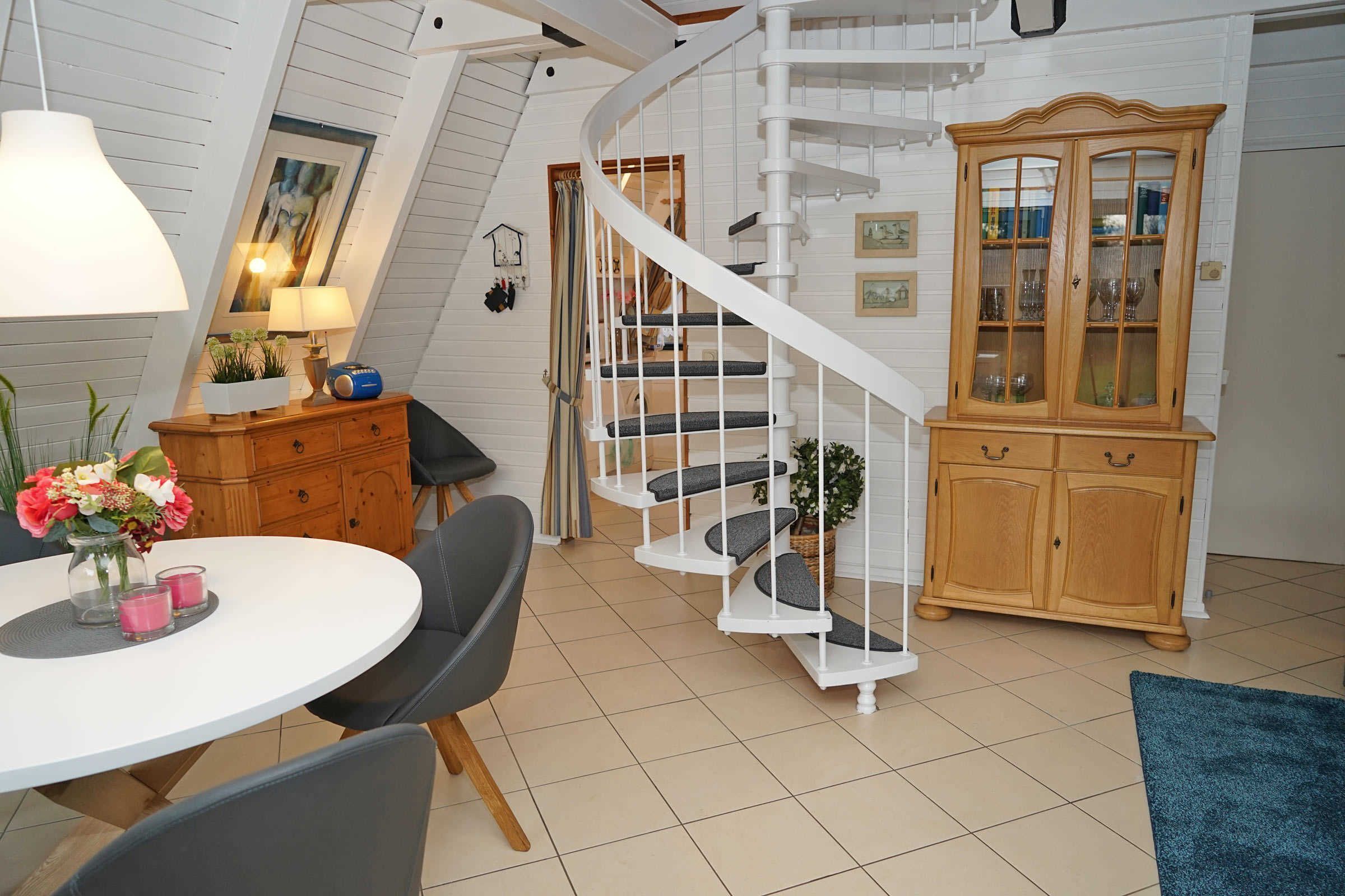 A spacious room with a white spiral staircase, a wooden cabinet with glass doors, and a round dining table with chairs.