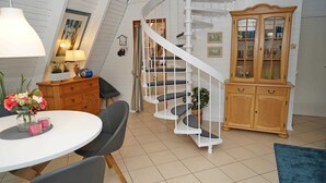 Een ruime kamer met een witte spiraaltrap, een houten kast met glazen deuren en een ronde eettafel met stoelen.