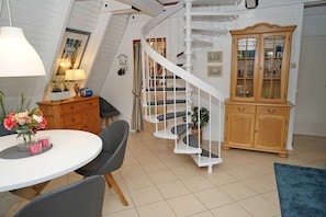 Ein geräumiger Raum mit einer weißen Wendeltreppe, einem Holzkabinett mit Glastüren und einem runden Esstisch mit Stühlen.