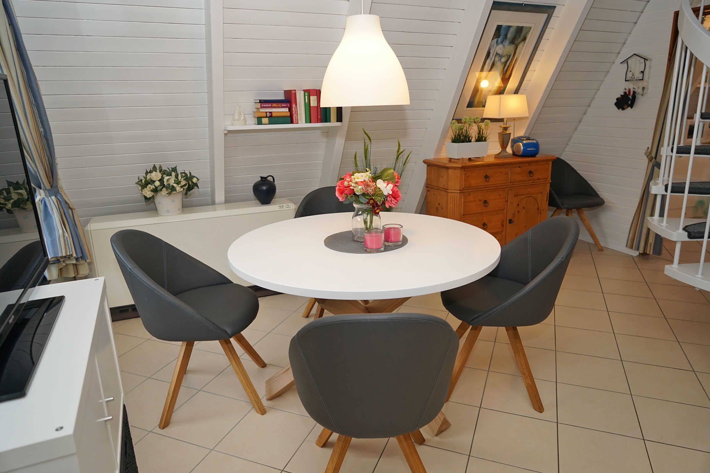 Een eetgedeelte met een ronde tafel, vier stoelen, een hanglamp, een boekenkast en een trap.