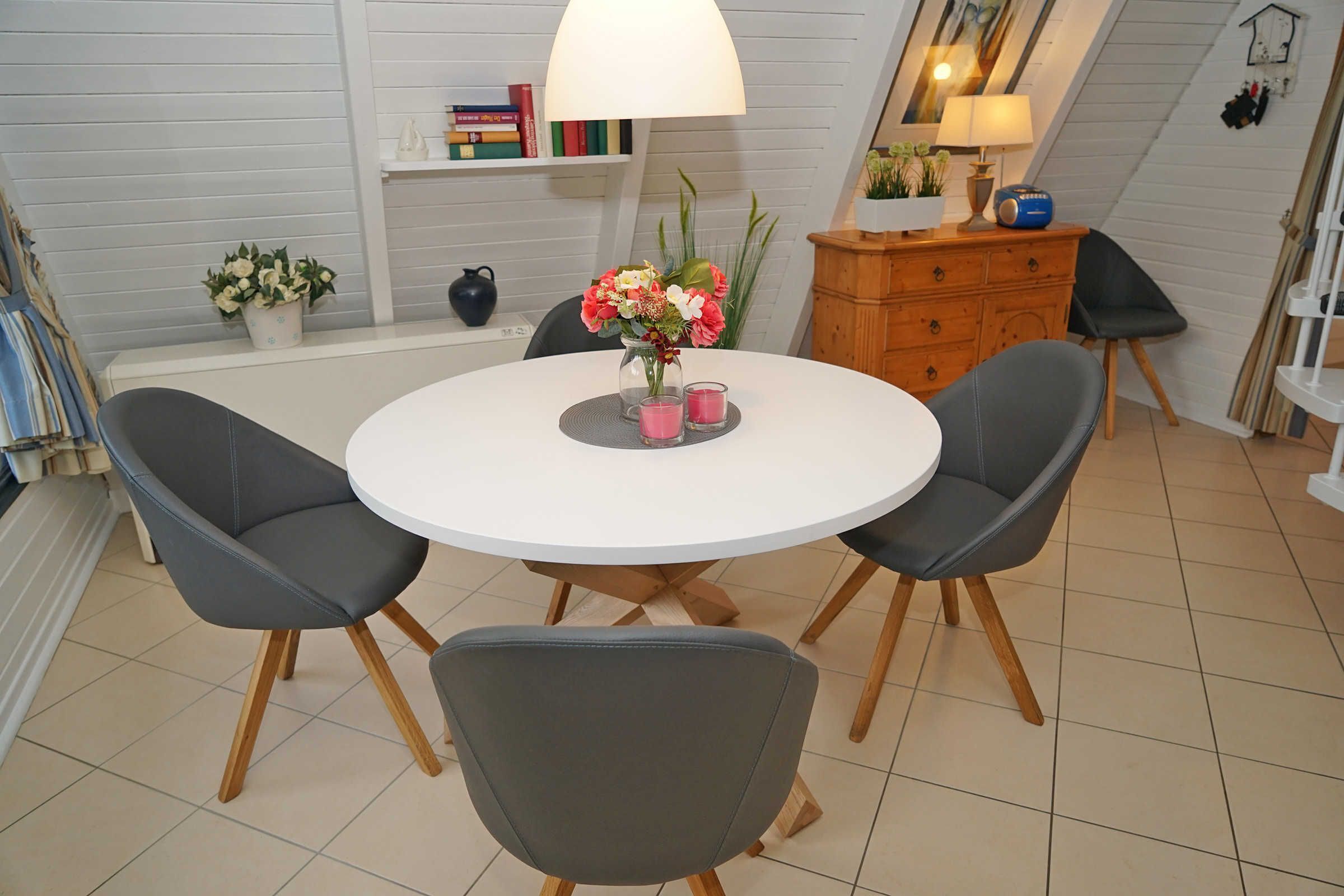 Een eetgedeelte met een ronde tafel, twee grijze stoelen, een witte lamp en een vaas met bloemen.