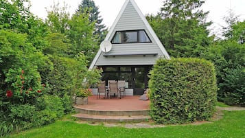 Una casa moderna con tetto triangolare, immersa nel verde e con patio arredato.