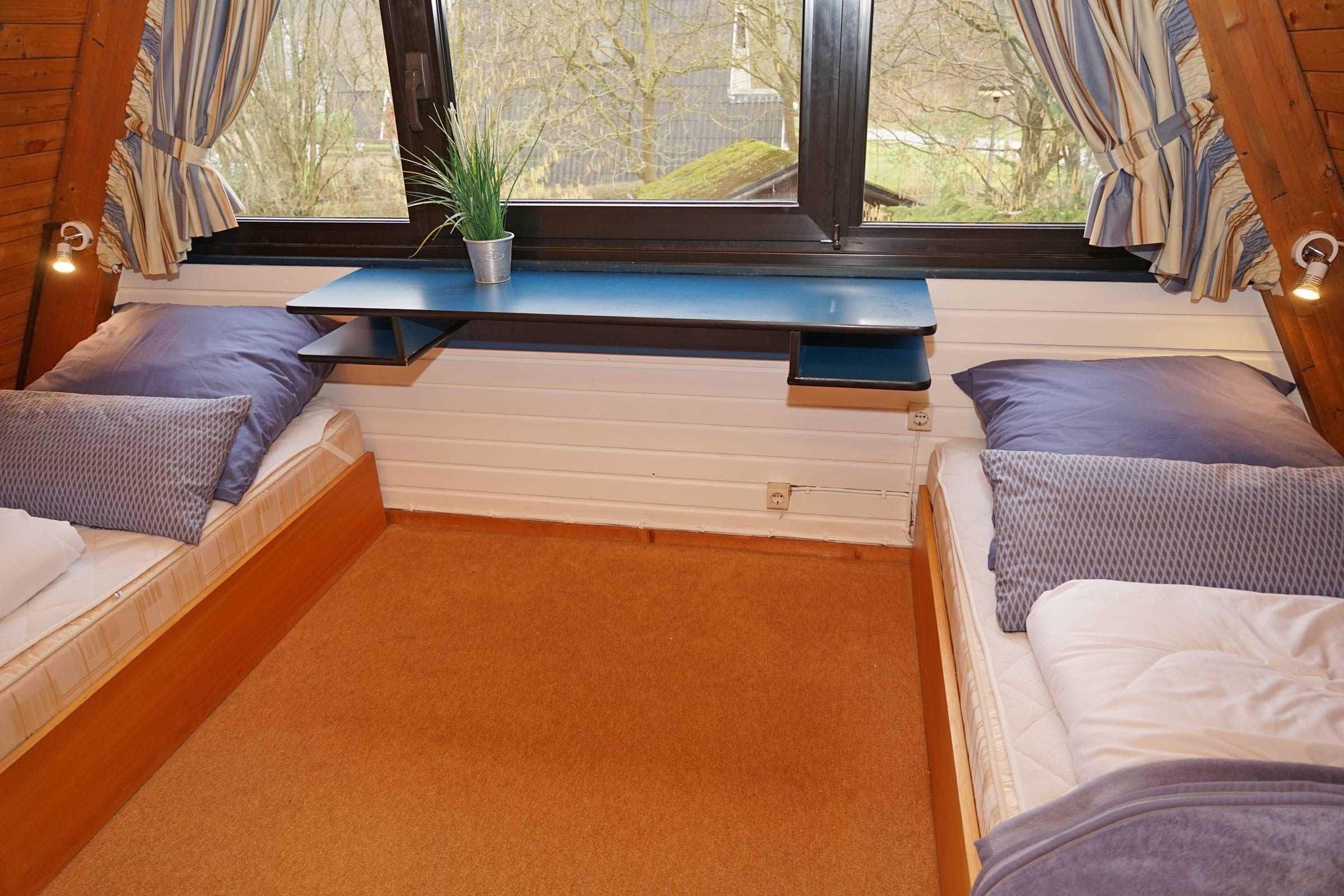 A cozy bedroom with two beds, a window with curtains, a small table, and a potted plant.