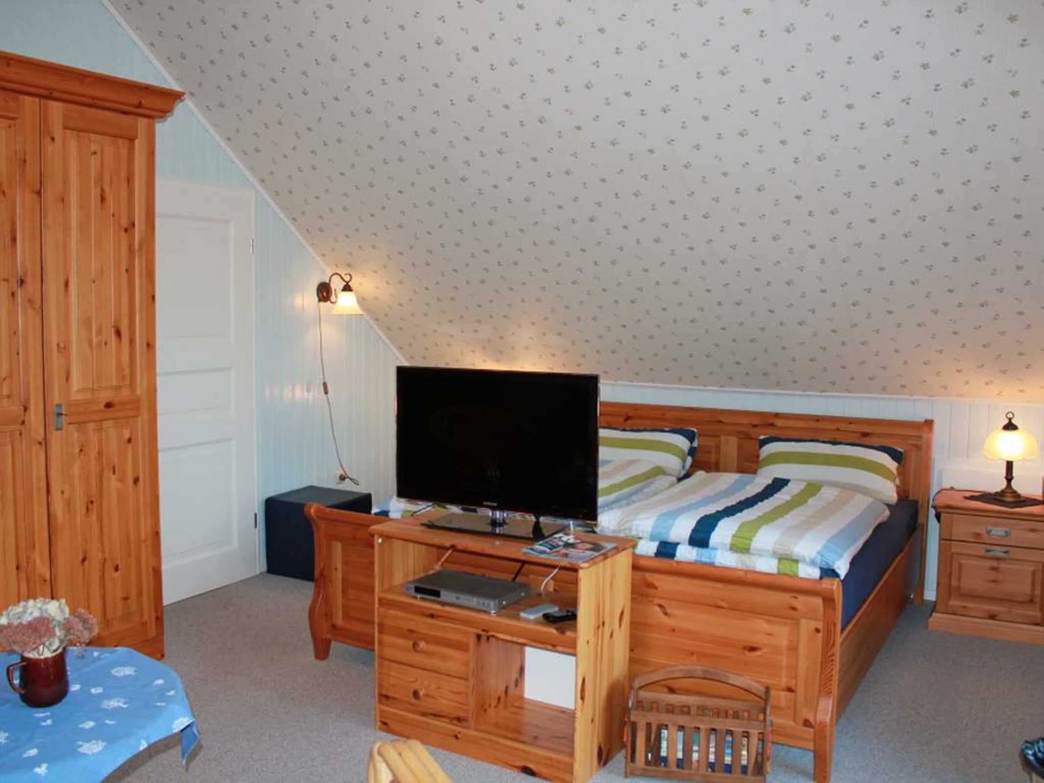 A bedroom with a wooden bed, a television on a wooden desk, and a small table with a vase.