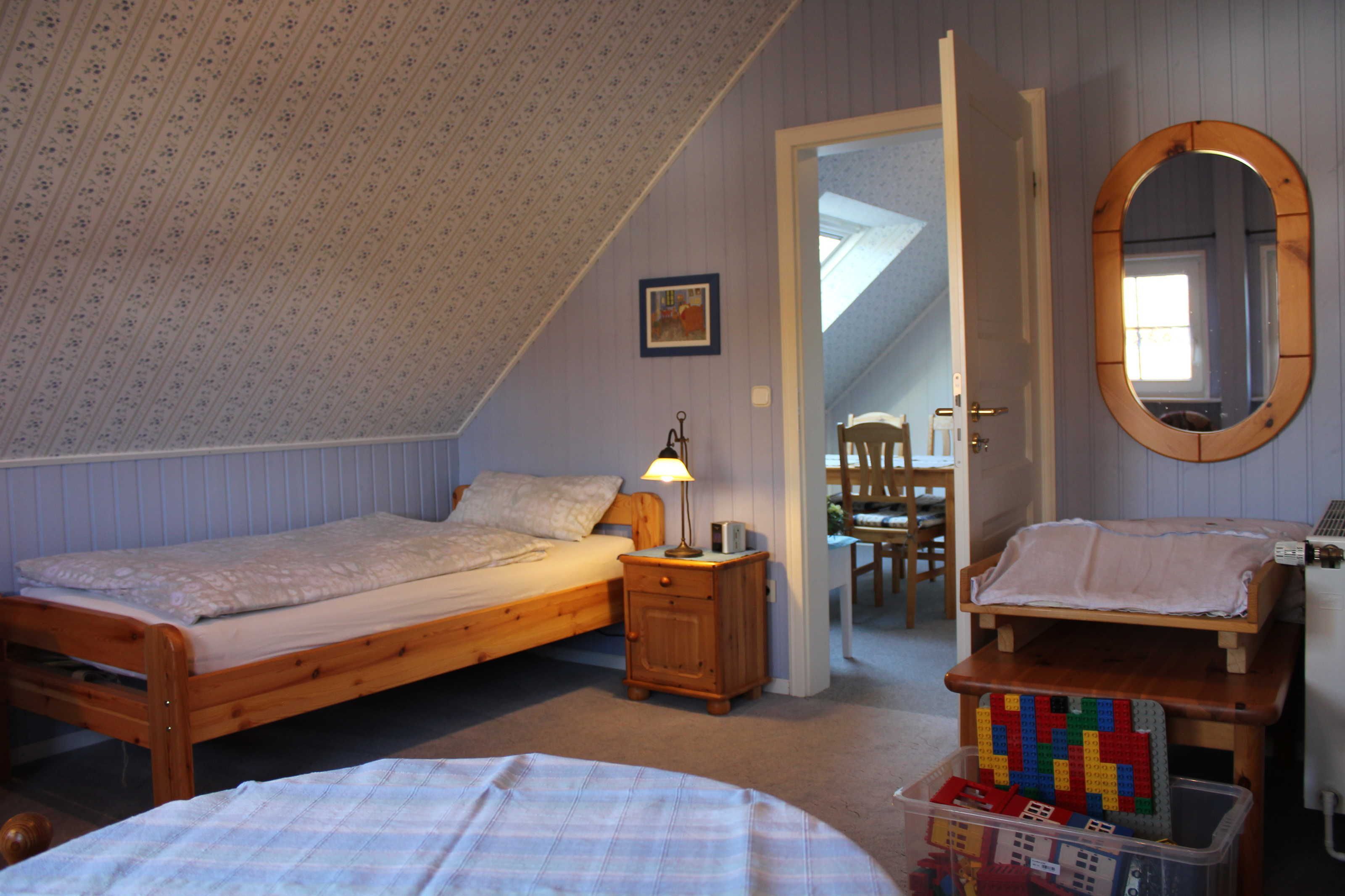 Ein Schlafzimmer mit zwei Einzelbetten, einem hölzernen Nachttisch, einem kleinen Tisch mit Lampe, einem Spiegel und einer Aufbewahrungsbox für Spielzeug.