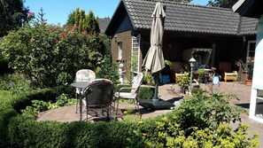 A patio area with outdoor furniture, a garden, and a house with a tiled roof.