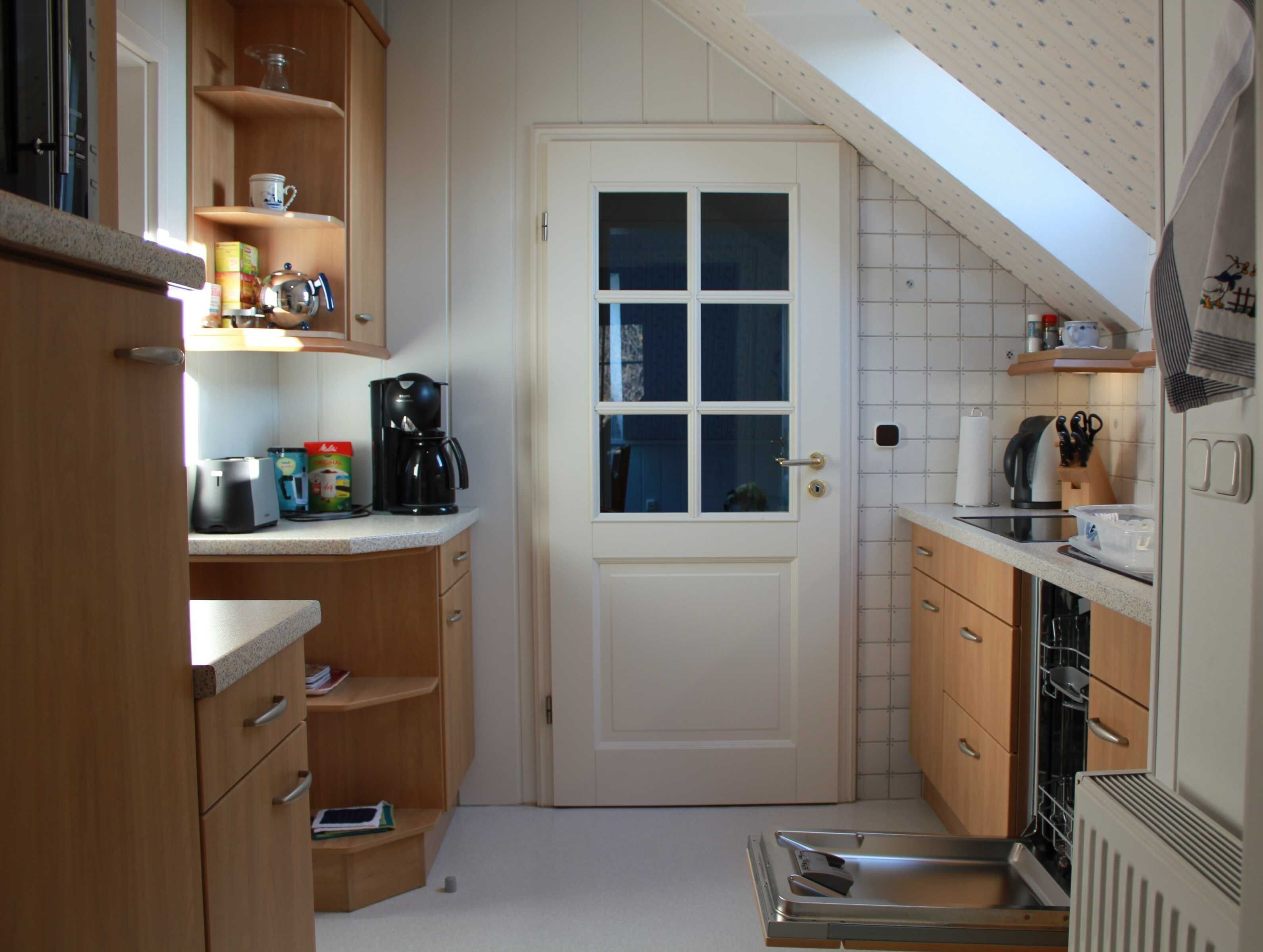 Een kleine keuken met houten kastjes, een koffiezetapparaat en een vaatwasser.
