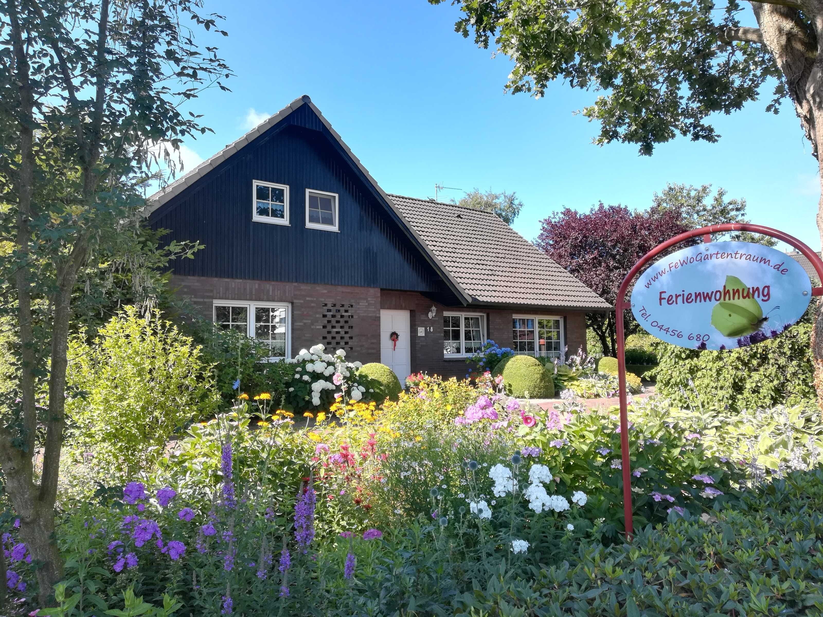 Ein Haus mit dunkelblauer Fassade, einem Ziegeldach und einem Garten mit verschiedenen Blumen und Sträuchern.