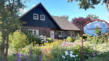 Una casa con facciata blu scuro, tetto in tegole e un giardino con fiori e arbusti diversi.